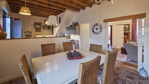 Un comedor con una mesa blanca, sillas de mimbre, piñas y un reloj en la pared.