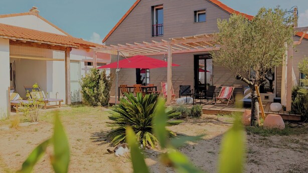 Una casa con un porche cubierto, un pequeño jardín y un paraguas rojo.