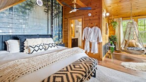 Une chambre dans une cabane en bois, avec un grand lit, un ventilateur de plafond et un fauteuil suspendu.