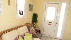 A room with a wicker sofa, a fire extinguisher, a door, and a tiled floor.