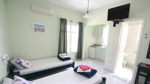 A room with two beds, a television, a kitchen area, and a bathroom visible through an open door.