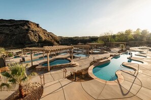 Un resort con varias piscinas, pérgolas y montañas al fondo.