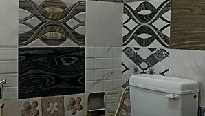 A bathroom with a toilet, a hand dryer, and a sink. The walls are tiled with various patterns and colors. - Wonder Inn Lodge (Ramanagara)