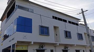 A multi-story building with a white facade, several windows, and visible air conditioning units.