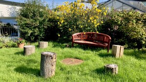 A garden with a wooden bench, surrounded by grass and flowering bushes. - Gemütliche Ferienwohnung Ganz nah am Fluss (Roding)