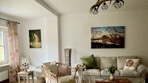 A cozy living room with a wicker chair, a sofa, a coffee table, and a painting on the wall. - Gemütliche Ferienwohnung Ganz nah am Fluss (Roding)
