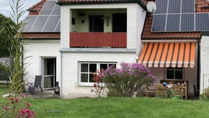 A two-story house with a red-tiled roof, solar panels, a balcony, and a garden with pink flowers. - Gemütliche Ferienwohnung Ganz nah am Fluss (Roding)