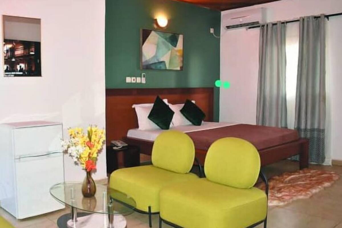 A hotel room with a bed, a glass table with a vase of flowers, and a green sofa.