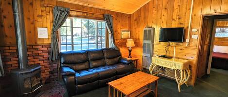 A cozy cabin interior with a leather sofa, a wooden table, a TV, and a fireplace.
