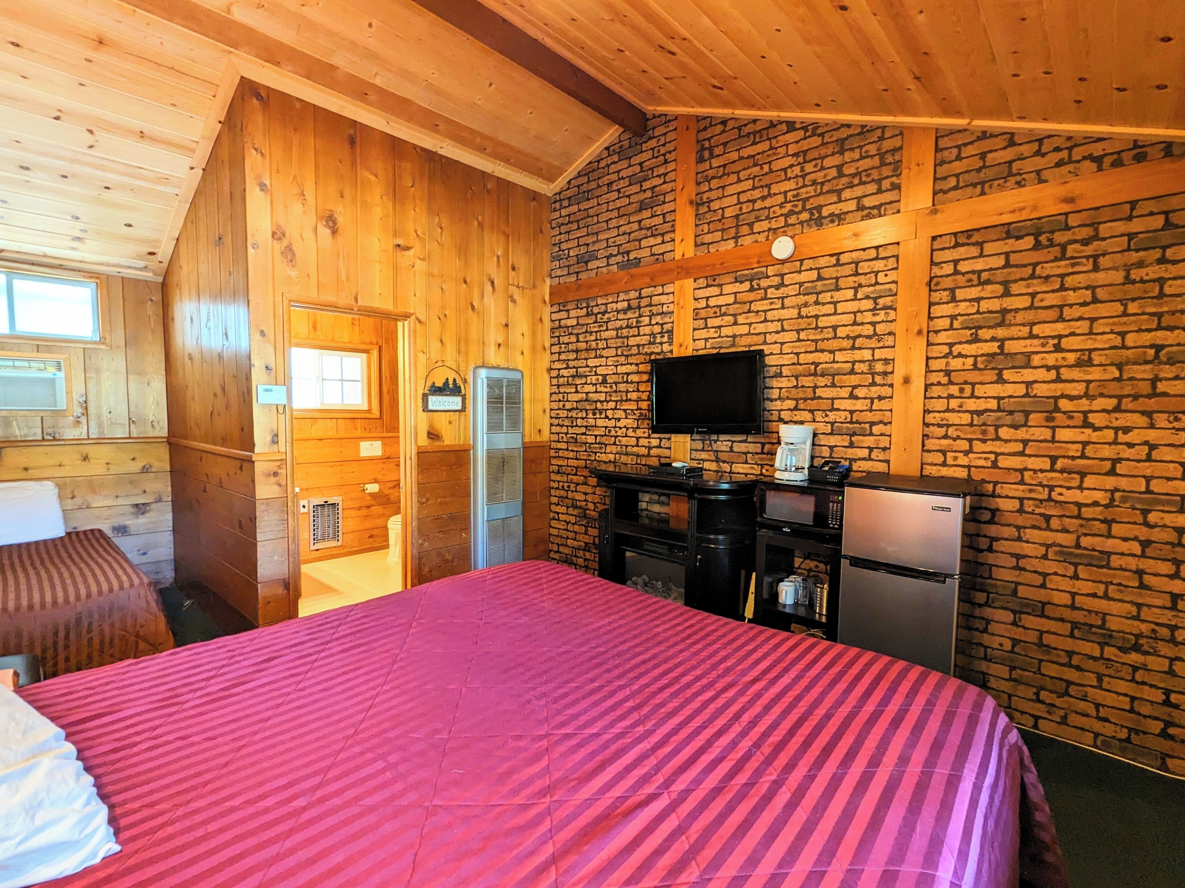 A room with a bed, a television, a coffee maker, and a refrigerator.