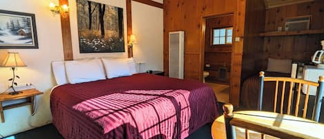 A wooden cabin-style bedroom with a large bed, a nightstand, a chair, and a painting on the wall.