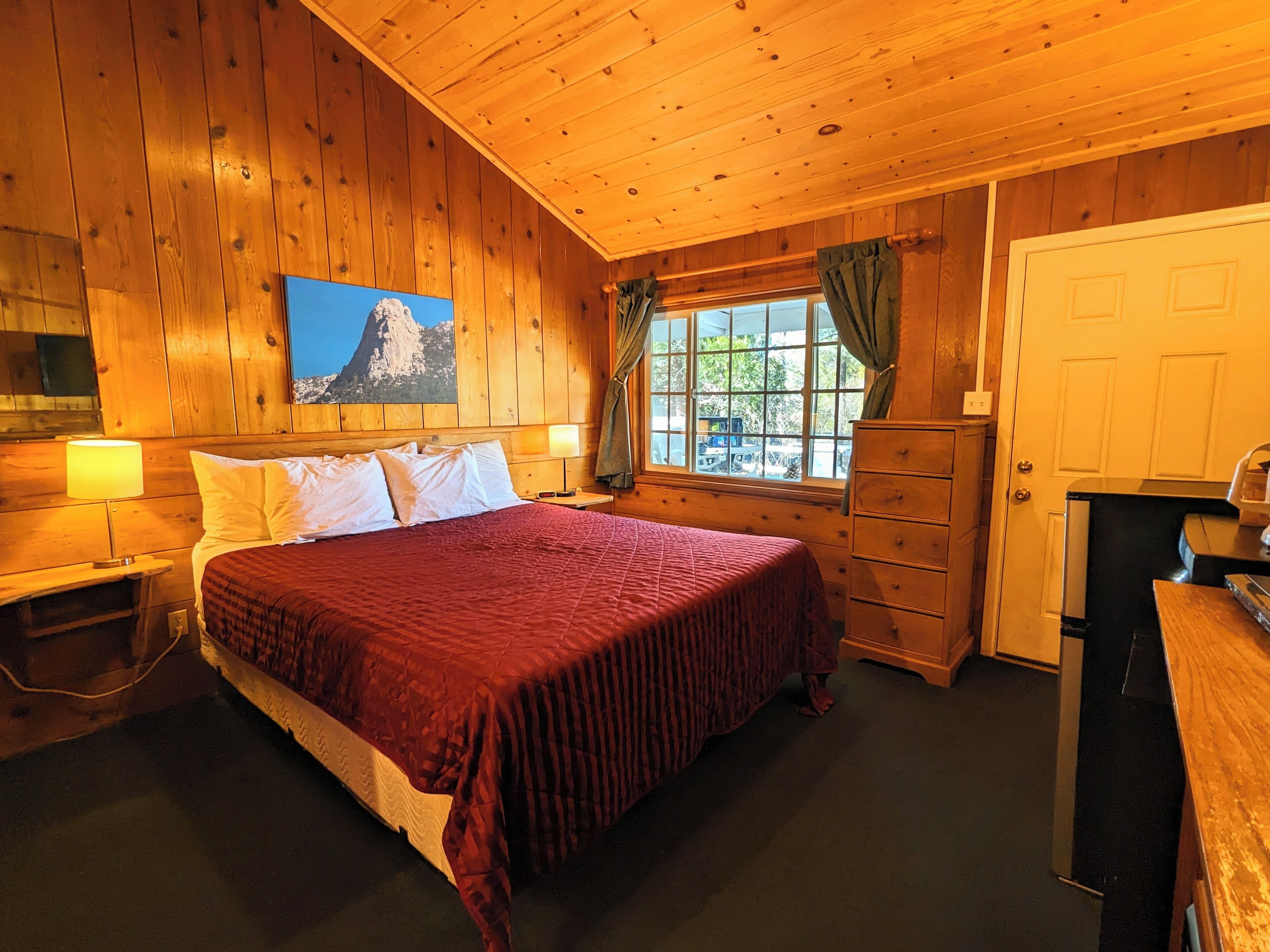 A wooden-paneled bedroom with a bed, dresser, and a window with curtains.