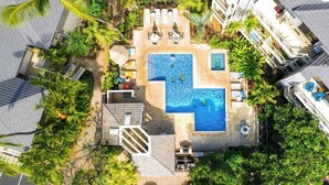 Vista aérea de un resort con una piscina central, rodeado de zonas de descanso y palmeras.