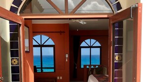 Una stanza con un letto, una panca e vista sull'oceano attraverso ampie finestre.