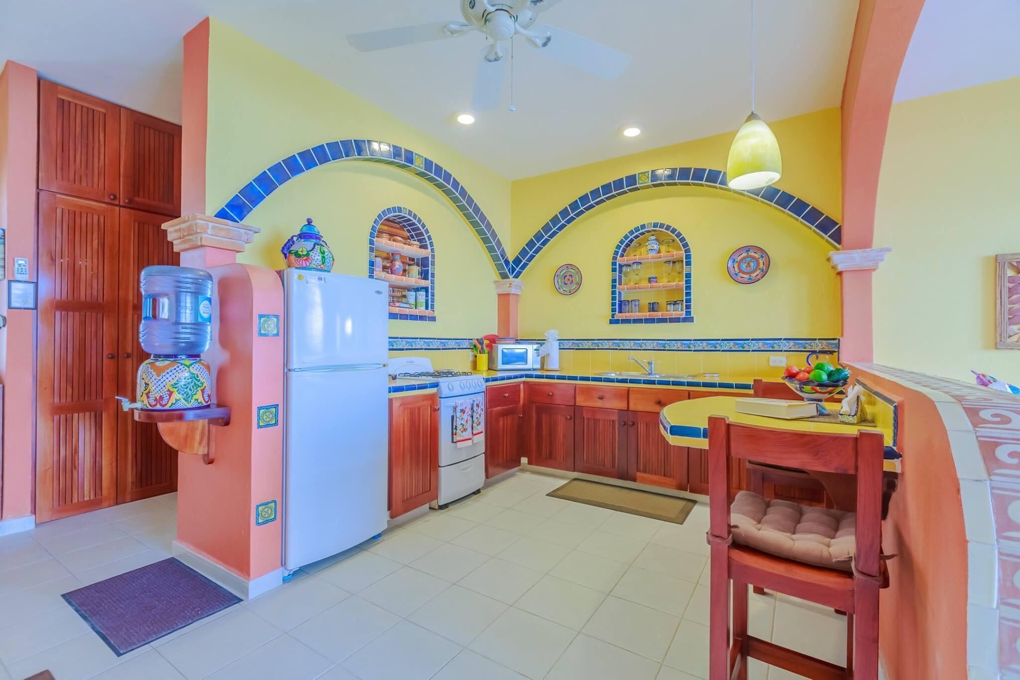 A kitchen with a microwave, stove, and refrigerator. There is a wooden cabinet and a chair.