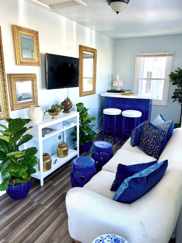 A modern living room with a white sofa, blue ottomans, and a TV on the wall.