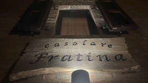 Ein hölzernes Schild mit dem Schriftzug 'casolare Fratina' an einer Ziegelwand, beleuchtet durch einen Scheinwerfer.