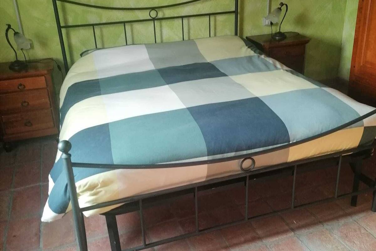 Un lit avec un matelas à carreaux dans une pièce aux murs verts et au sol carrelé.