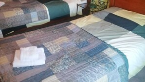 Ein Zimmer mit zwei Betten, jedes mit einer gesteppten Bettdecke und einem weißen Handtuch auf dem Boden. Es gibt einen Holzschrank und ein an der Wand hängendes Bild.