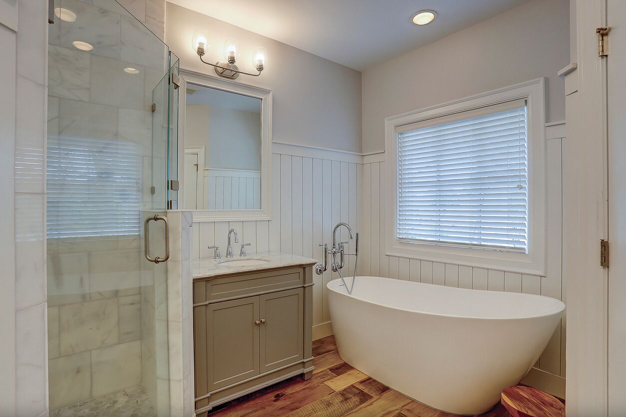 Une salle de bain avec une baignoire sur pieds, une douche à parois de verre, un meuble-lavabo et une fenêtre avec des stores.
