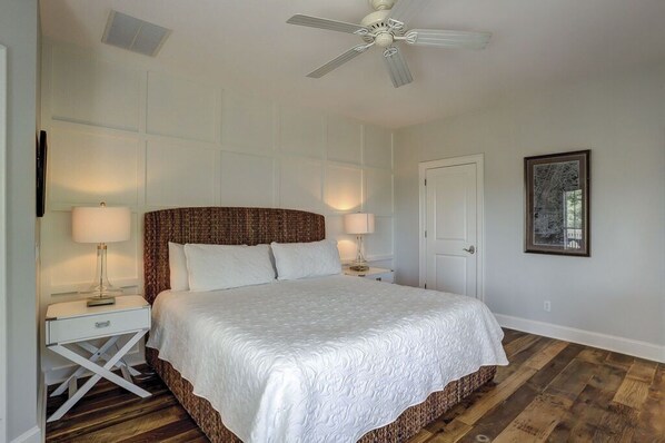 A bedroom with a large bed, two bedside tables with lamps, a ceiling fan, and a framed picture on the wall. - 7 Bayberry - 2nd Row, 6BR/6.5BA, Fully Renovated, Steps from the Beach, Pool (Hilton Head Island)