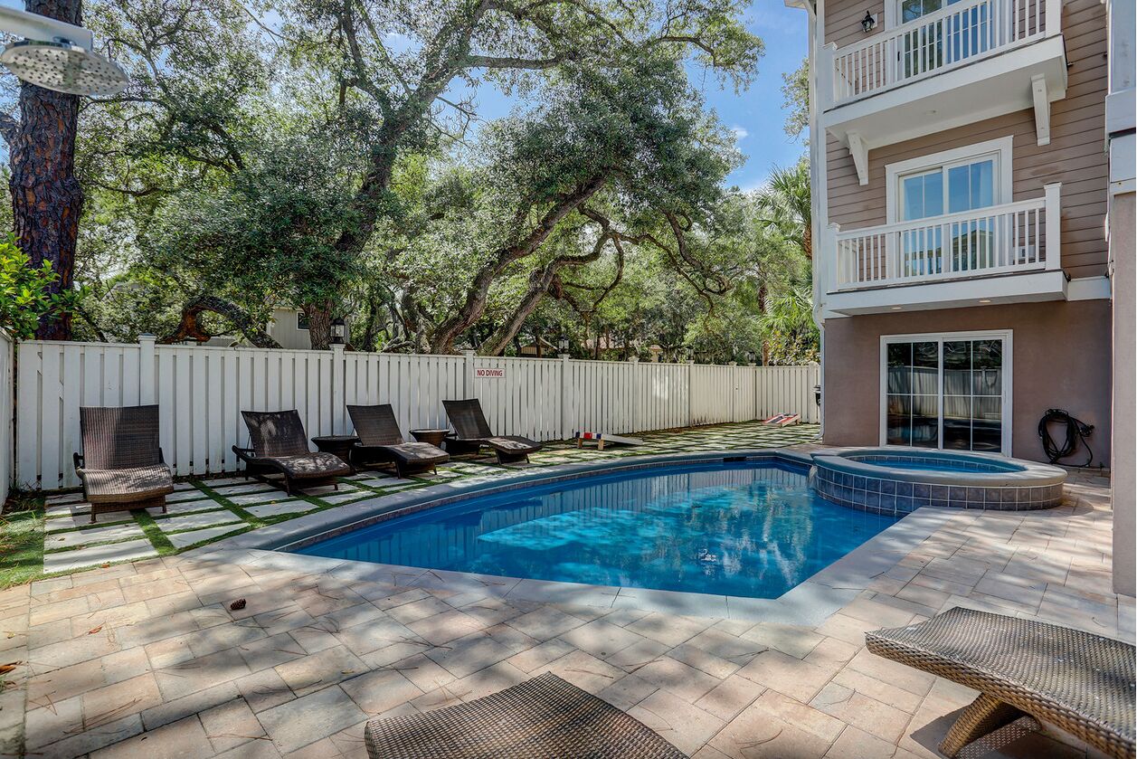 A swimming pool with lounge chairs, a hot tub, and a white fence.