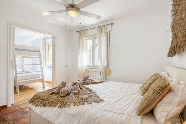 A bedroom with a bed, a ceiling fan, a window with curtains, and a door leading to another room.