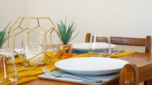 Une table à manger dressée avec une assiette blanche, un verre, un vase géométrique doré et une petite plante dans un pot en cuivre.