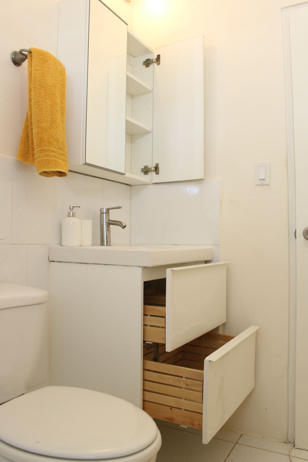 A bathroom with a toilet, a sink with a mirror above it, and a towel hanging on the wall.