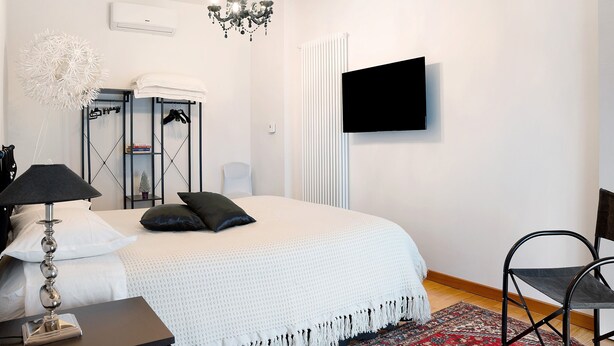 Un dormitorio con cama, televisor, candelabro, radiador y una silla.