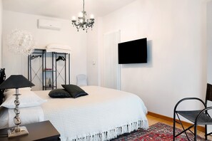 Ein Schlafzimmer mit Bett, Fernseher, einer Kristallleuchtre, einer Heizung und einem Sessel.