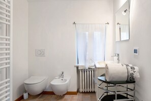 Casa de banho com sanita, bidé, lavatório e porta-toalhas.
