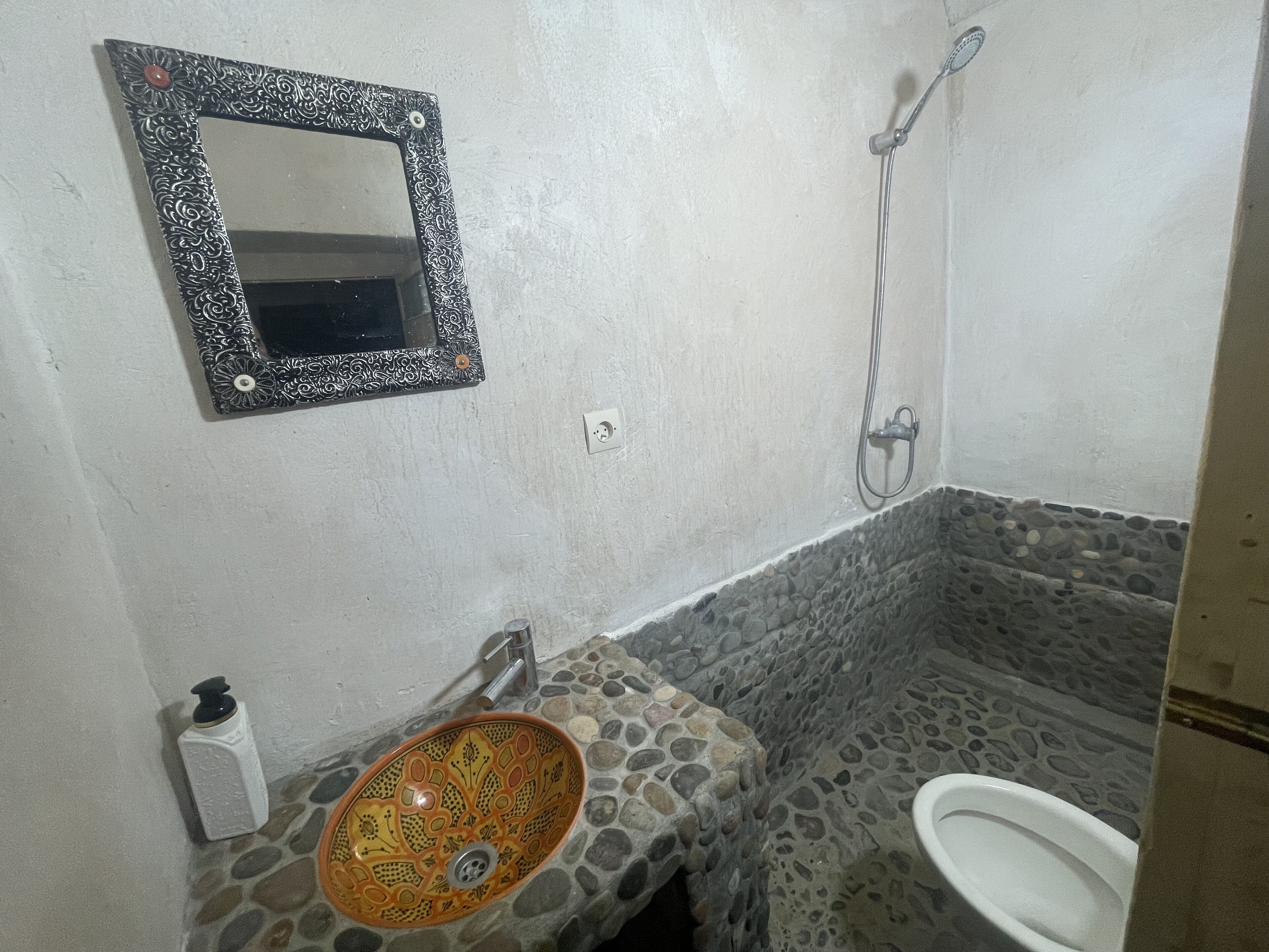Un baño con lavamanos de piedra, inodoro, ducha y espejo con marco decorativo.