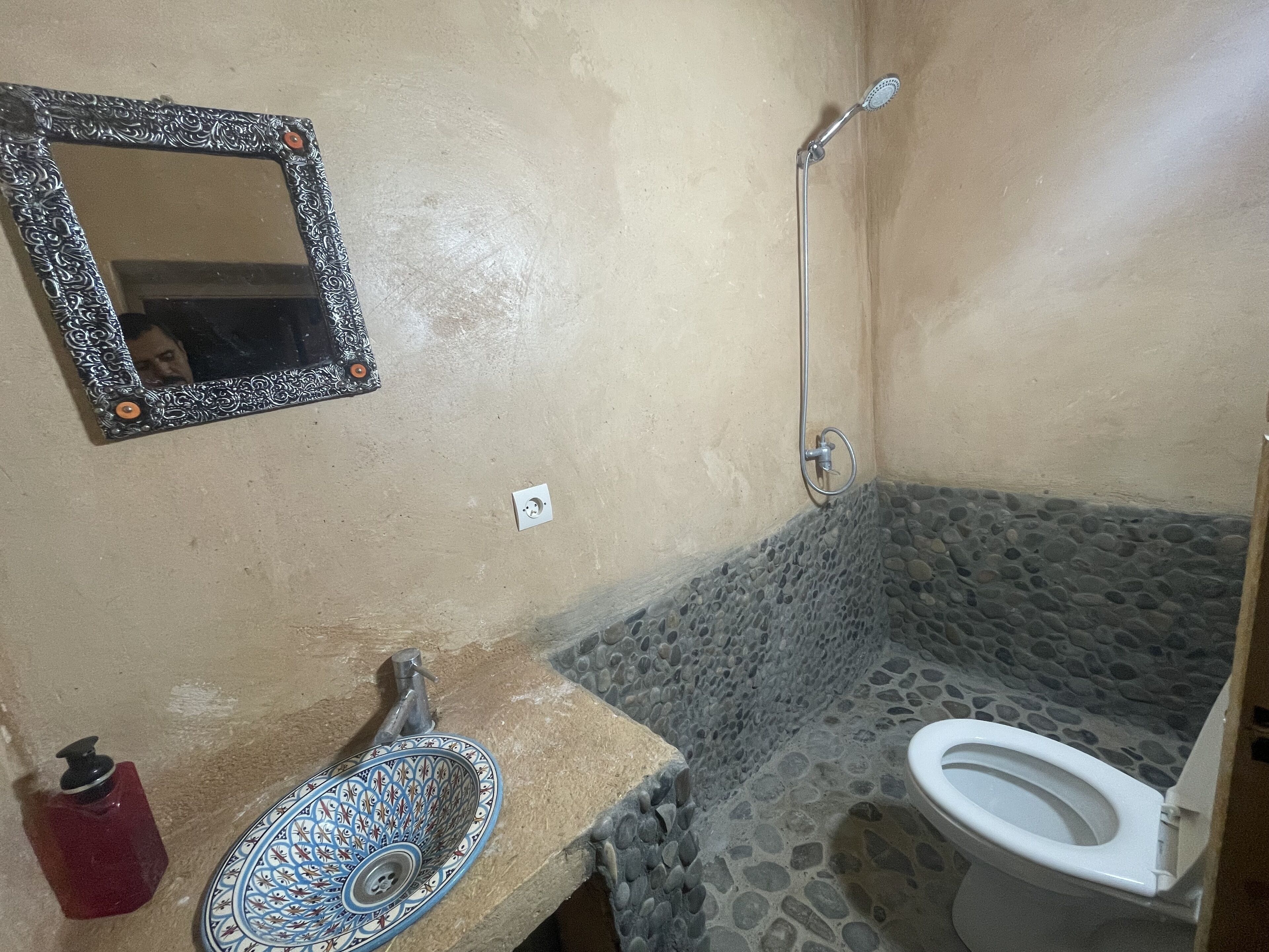 Une salle de bain avec une douche carrelée en pierre, un lavabo doté d’un receveur décoratif et des toilettes.
