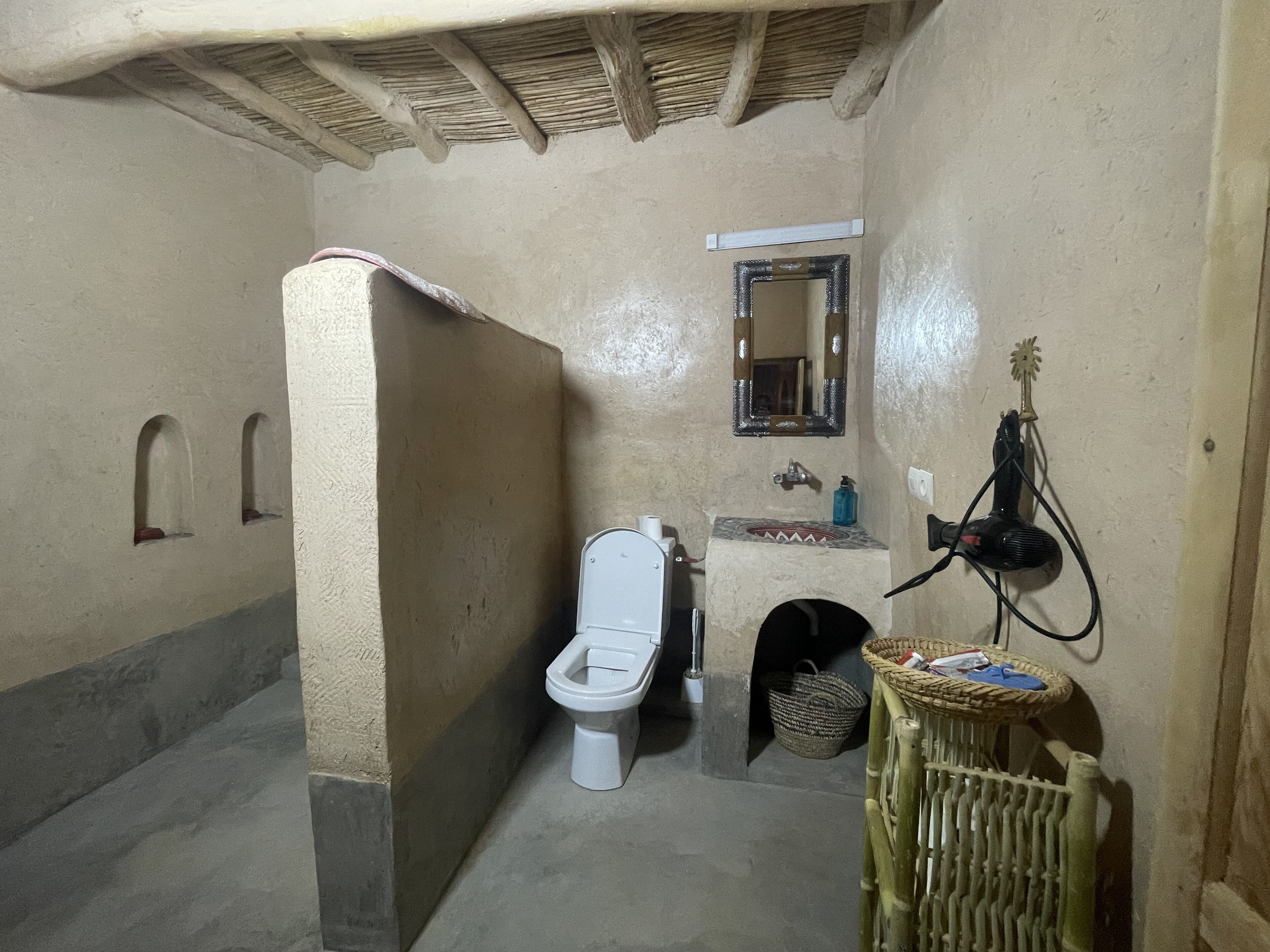 Un baño pequeño con inodoro, lavamanos, espejo y una cesta.