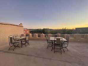 An outdoor patio with a table and chairs, a stone wall, and a view of the landscape. - Maroc des Merveilles - Chez l'habitant (Ait Sedrate Sahl El Gharbia)