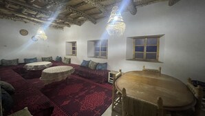 A traditional room with a wooden ceiling, a round wooden table, and a patterned red carpet. - Maroc des Merveilles - Chez l'habitant (Ait Sedrate Sahl El Gharbia)