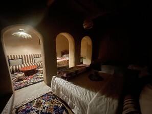 A dimly lit room with a sofa, a bed, and a small table. There are two arches in the room, and a colorful rug is visible on the floor. - Maroc des Merveilles - Chez l'habitant (Ait Sedrate Sahl El Gharbia)