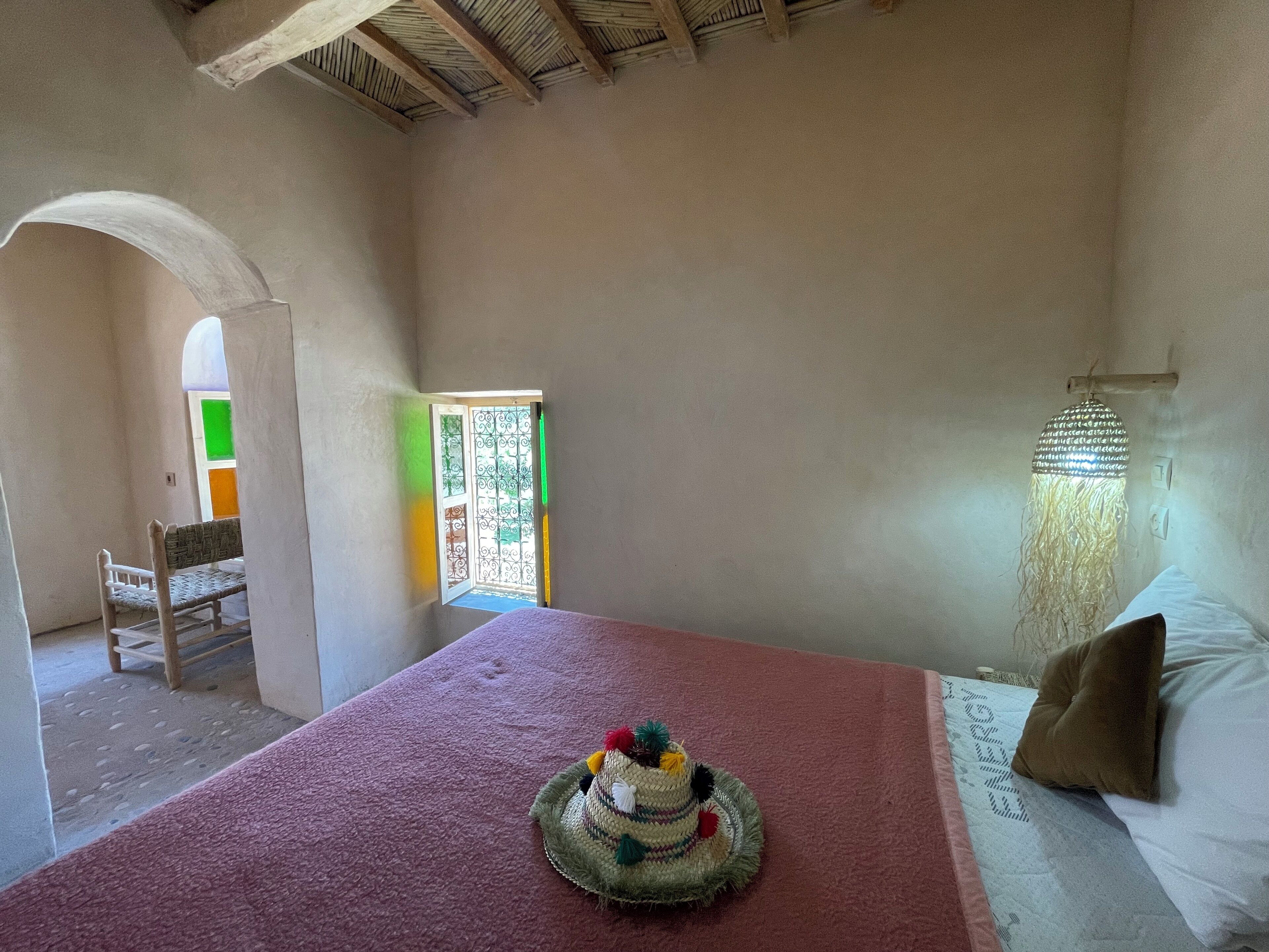 A room with a bed, a red carpet, a decorative hat, a chair, and a window with a green and orange view.
