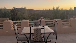 A table and chairs set on a terrace with a view of a hilly landscape and a sunset. - Maroc des Merveilles - Chez l'habitant (Ait Sedrate Sahl El Gharbia)