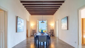 A spacious hallway with a dining area, wooden beams on the ceiling, and framed artwork on the walls.