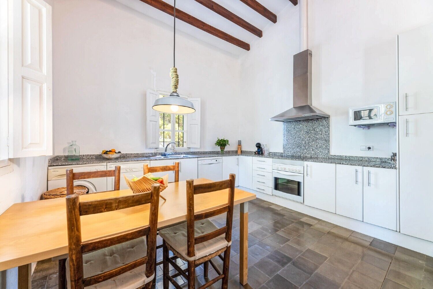 Una cocina con armarios blancos, una mesa de comedor de madera y una lámpara colgante.