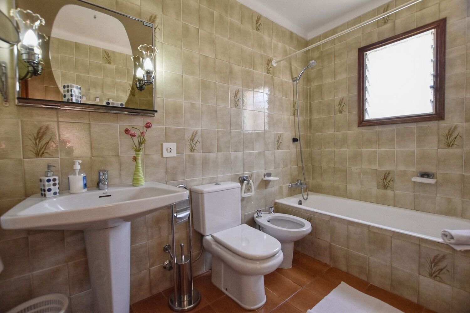 Ein Badezimmer mit Waschbecken, Toilette, Bidet und Badewanne, inklusive Spiegel und Wandleuchte.