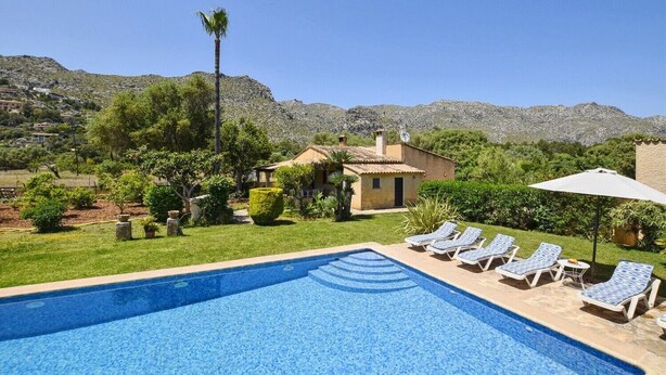 Une piscine avec des chaises longues, une maison et un paysage montagneux en arrière-plan.