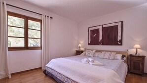 Une chambre à coucher avec un grand lit, deux tables de chevet avec des lampes, une fenêtre avec des rideaux et un tableau au mur.