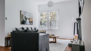 Ein modernes Wohnzimmer mit einem dunkelgrauen Sofa, einem Holztisch und einem großen Fenster mit Blick auf Bäume.