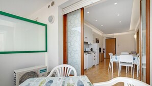 A dining area with a table set for four, a kitchen in the background, and a sliding glass door leading to another room. - Apartment 'Residence Papaya A202' with Shared Pool and Private Terrace (Jesolo)