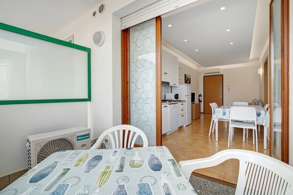 Un comedor con una mesa preparada para cuatro, una cocina al fondo y un ventanal corredero que da a otra habitación.