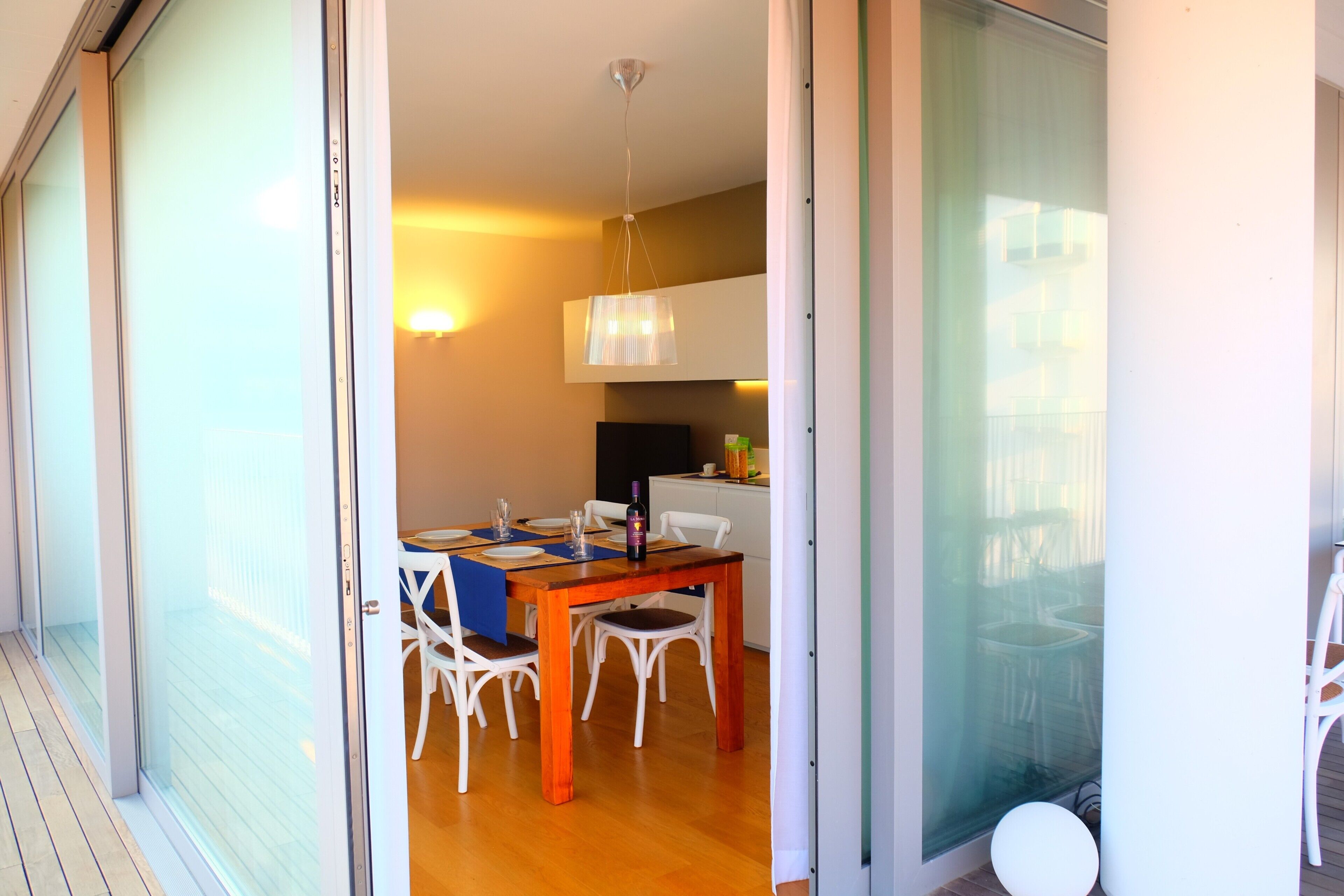 Comedor con mesa de madera, sillas blancas y lámpara colgante.