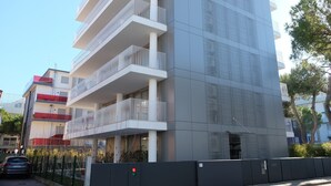 A multi-story building with balconies, a gated entrance, and a clear sky. - Apartment 'Residence Shine 06' with Private Terrace and Air Conditioning (Jesolo)